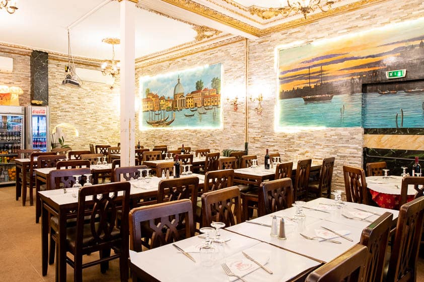 La salle du Bistrot Venezia : tables dressées, corniche dorée et peintures de Venise sur les murs de pierre.