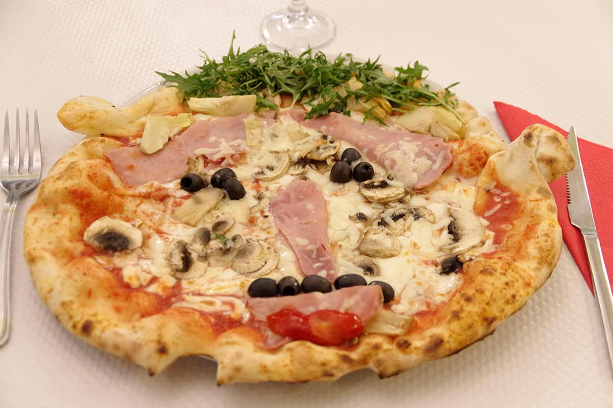 Pizza Quatre saisons : mozzarella, jambon, champignons, artichauts et olives, servie avec de la roquette.